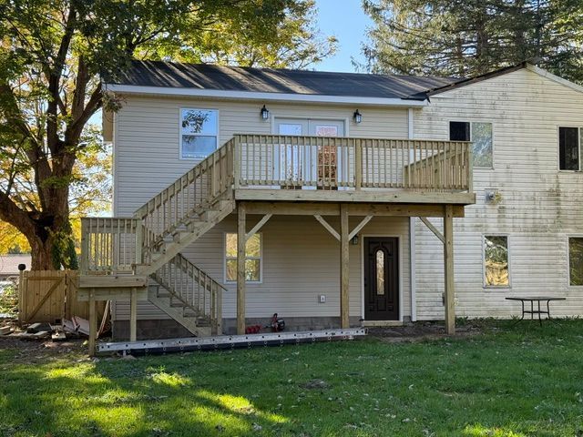 Two-story house with exterior wooden staircase, upper deck, and grassy yard.