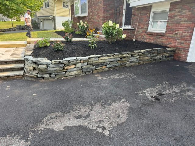 Stone retaining wall with mulch bed beside a driveway and front steps by a house