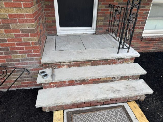Brick stoop with three worn concrete steps, black railing, and a white door entrance.
