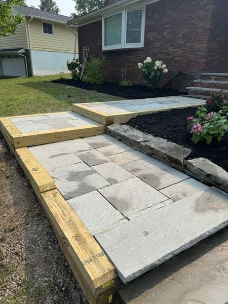 Uneven concrete pavers and wooden forms for a front walkway beside a brick house.