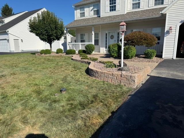 Suburban house with front lawn, stone planter, and driveway on a sunny day