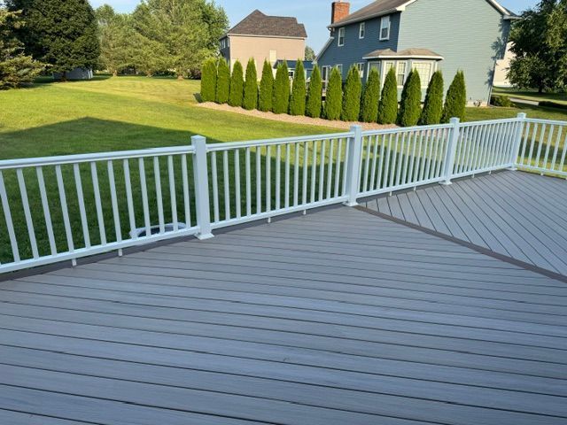 Gray deck with white railing overlooking a green lawn and suburban houses.