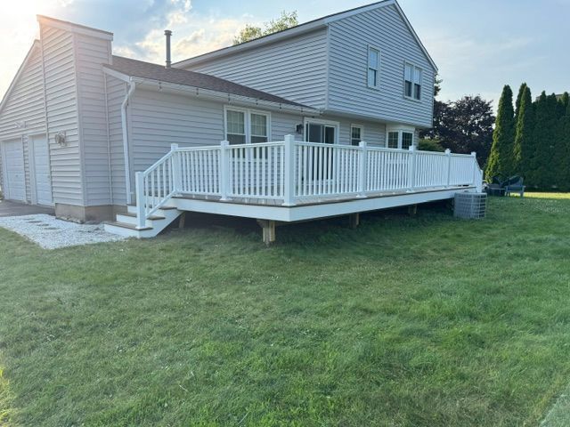 Backyard deck with white railing attached to a gray house on a grassy lawn