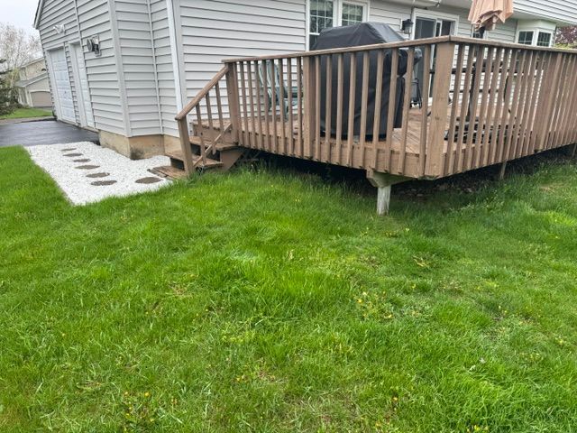 Wooden deck attached to a gray house beside a green lawn and stepping stones.