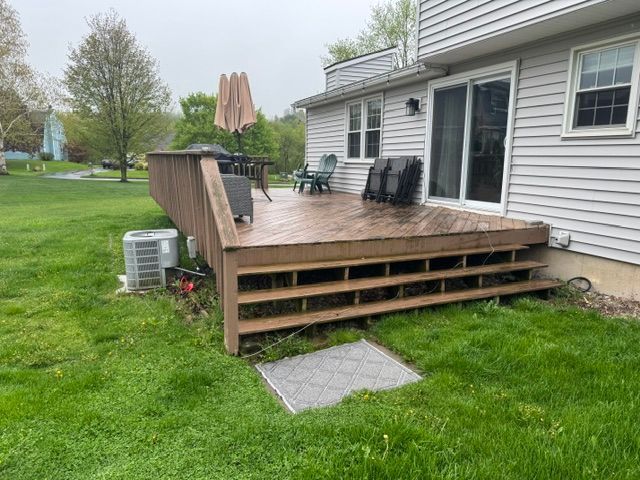 Wooden backyard deck with steps beside a house, patio umbrella, and grill on a grassy lawn