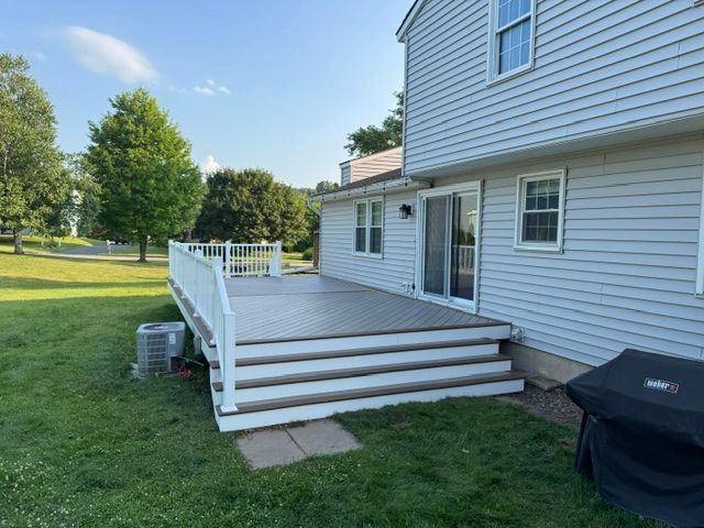 White wooden deck with steps beside a gray house on a grassy lawn