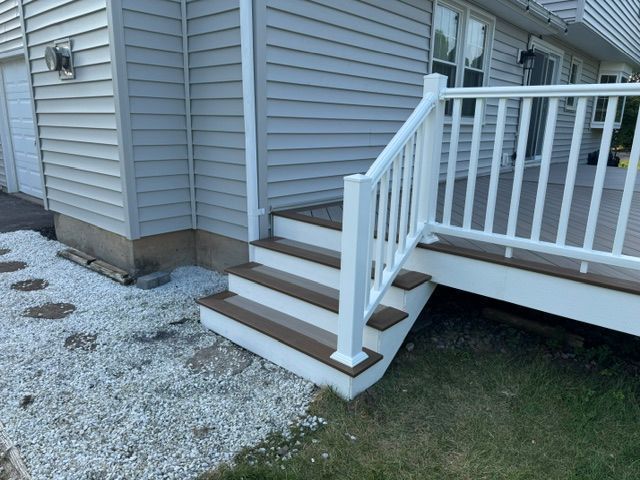 House exterior with small white-railed steps leading up to a raised deck beside gravel and grass.