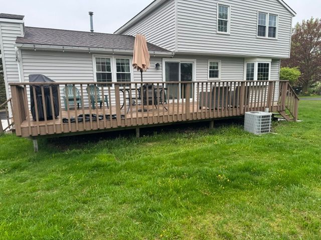 Backyard deck attached to a house, with patio furniture, umbrella, and air conditioner unit on the lawn