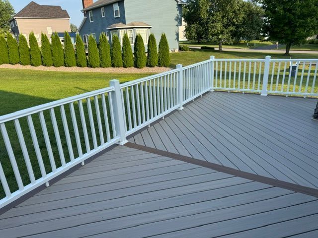 White-railed gray deck overlooking a green lawn and row of shrubs in a suburban backyard