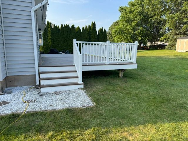 White backyard deck stairs with railing beside a house and lawn under a blue sky
