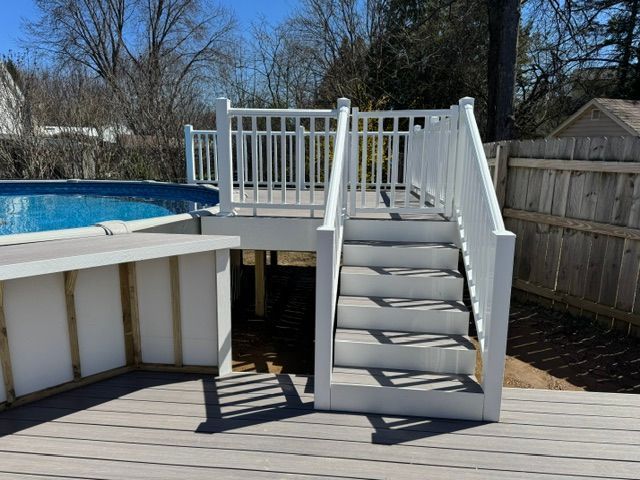Backyard above-ground pool deck with white railing and steps leading down to the patio