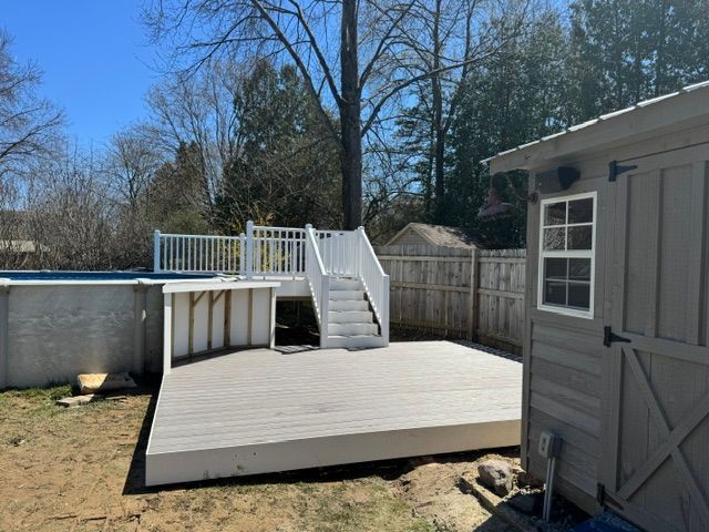 Backyard deck with white railings and stairs beside a gray shed on a sunny day