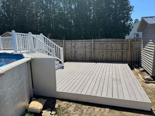Backyard deck beside above-ground pool, with white railings and fenced yard in sunlight