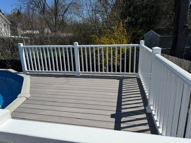 White deck with railing beside an above-ground pool, overlooking a backyard.