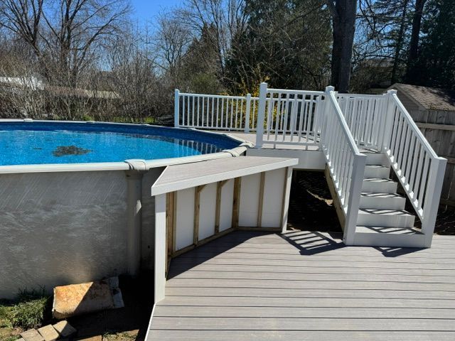 Backyard pool with white deck stairs and railing beside a wooden deck, trees in the background