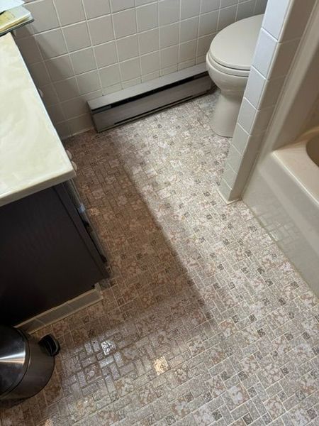 Small bathroom with tile floor, toilet, sink vanity, and trash can.