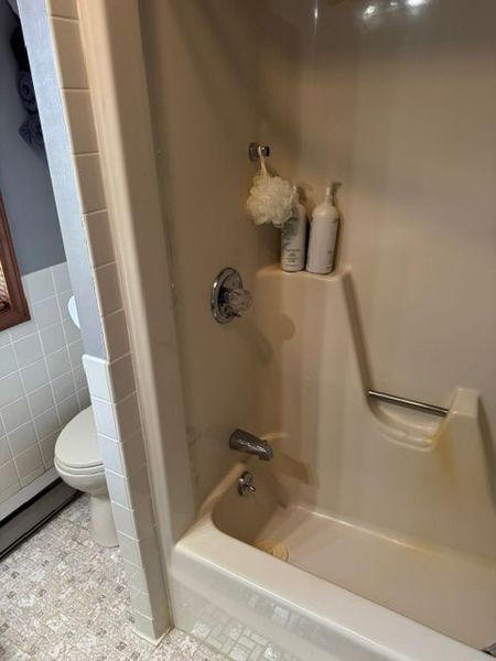 Accessible shower and tub with grab bar, built-in shelf, and bath items in a beige bathroom