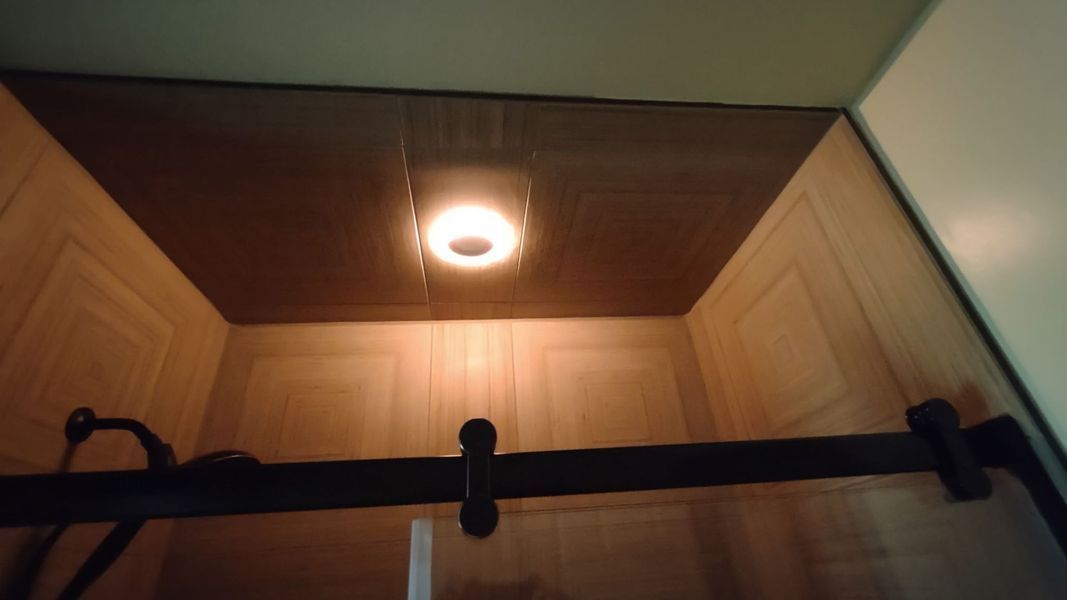 Ceiling light above a black shower curtain rod in a bathroom.
