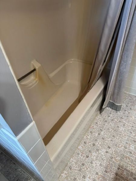 Empty beige shower stall with curtain and tiled bathroom floor