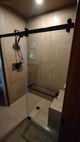 Glass shower door with a black top bar and chrome support, viewed in a tiled bathroom