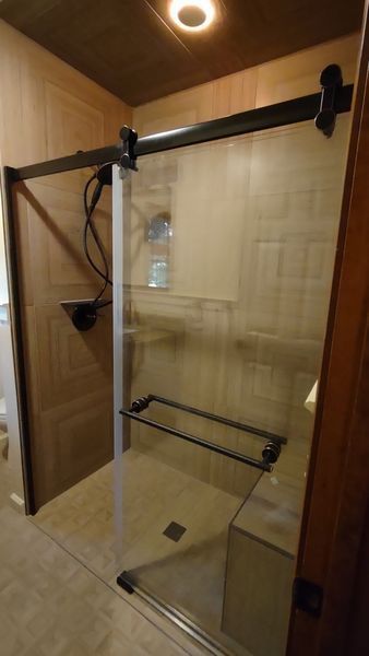 Glass shower enclosure with black towel bars in a beige tiled bathroom