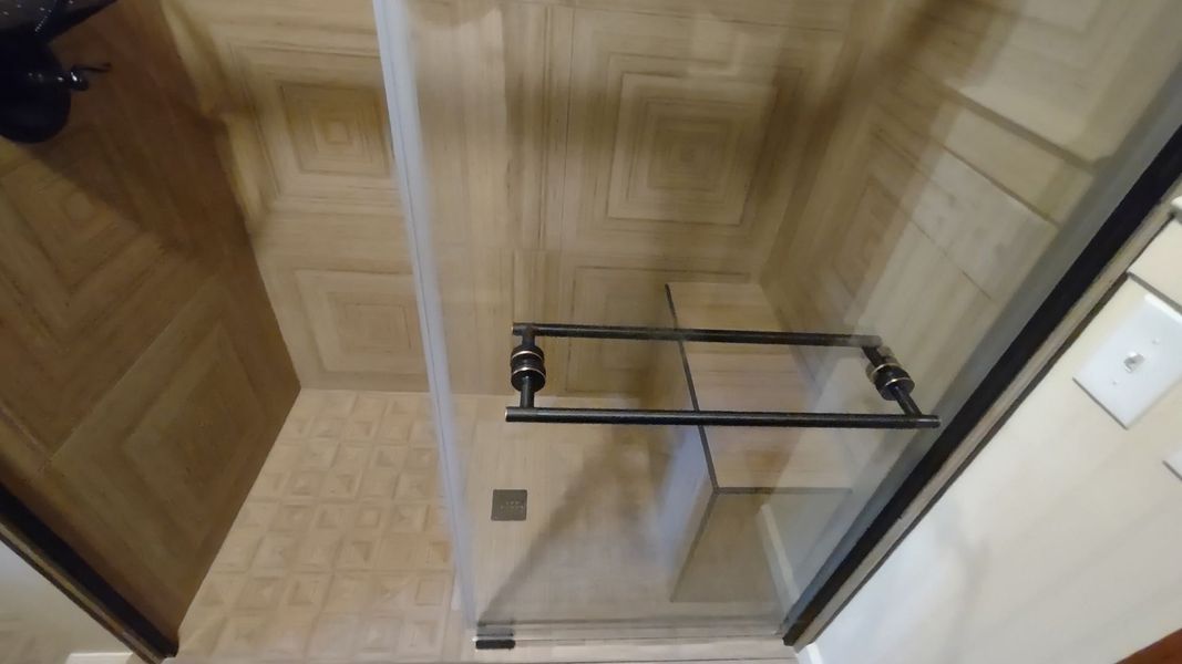Glass shower enclosure with chrome towel bar in a beige-tiled bathroom