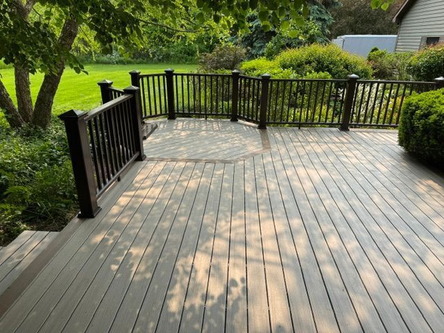 Wooden backyard deck with black railings, surrounded by green trees and shrubs