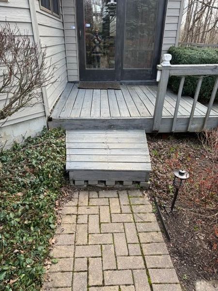 Front steps and porch with a small wooden ramp leading to a glass door, above a brick walkway.