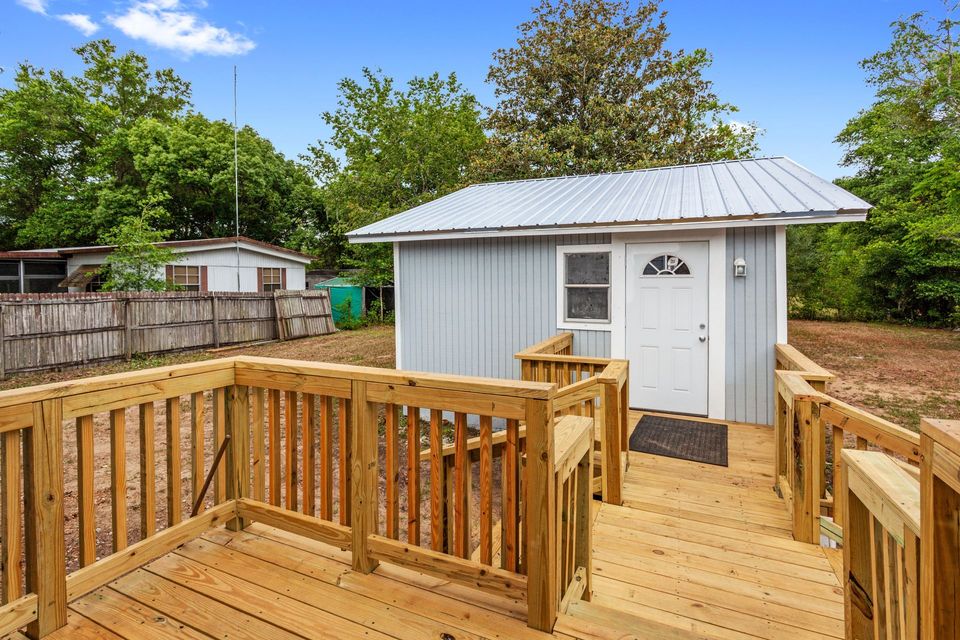 Wooden deck leading to a small gray shed with white doors in a backyard.