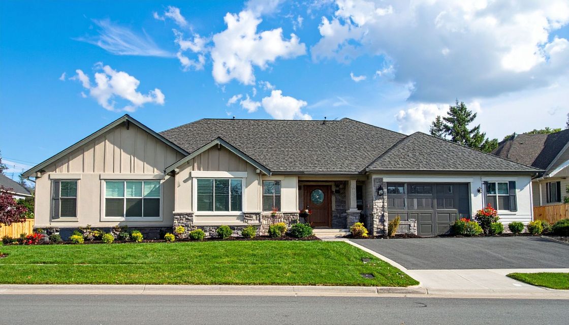 Single-story suburban house with a gray roof, front lawn, and driveway under a blue sky.