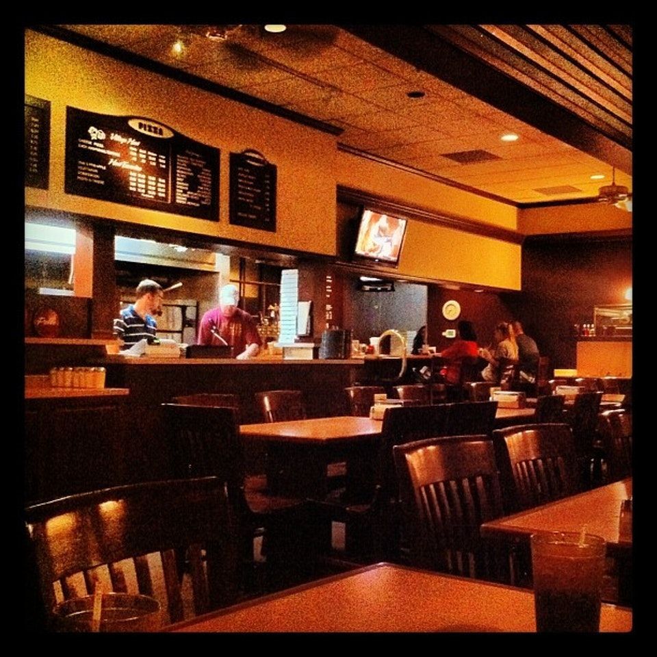 Dimly lit restaurant interior with menu boards, counter staff, and empty tables under warm orange lighting