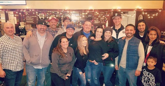Group of people posing together indoors at a warmly lit restaurant or bar, smiling at the camera.