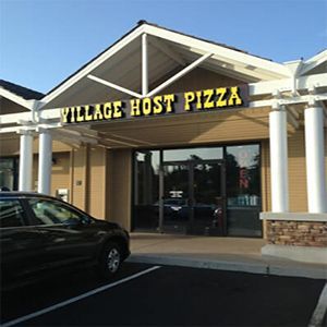 Village Host Pizza storefront with yellow sign, beige awning, and parked car outside