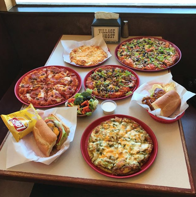 Several pizzas and sandwiches arranged on a table in a restaurant booth