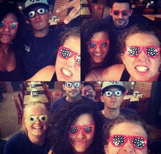 Group selfie in a restaurant, people wearing colorful sunglasses and smiling at the camera.