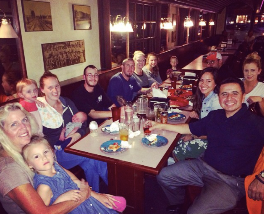 Group of people gathered around a restaurant table, smiling and dining in a warmly lit booth.