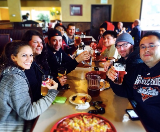 Friends raising beer glasses around a table with pizza in a cozy restaurant