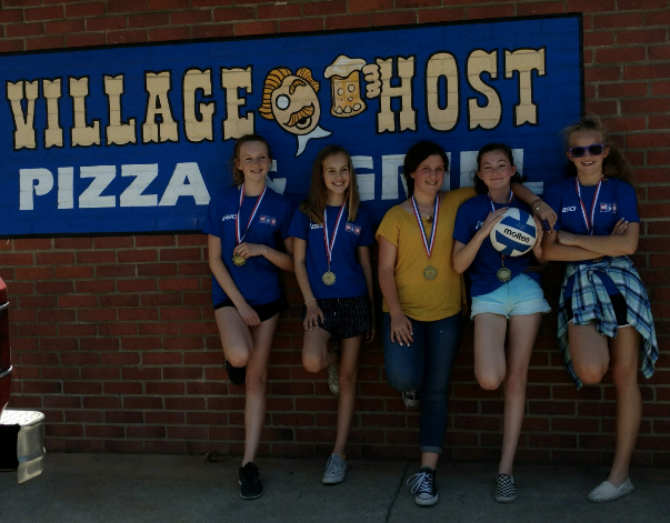 Five people posing outside Village Ghost Pizza sign, holding drinks and smiling.