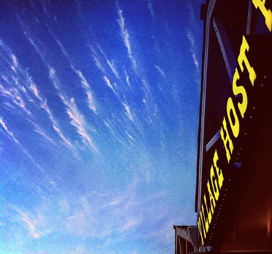 Blue sky with streaky clouds beside a building with yellow signage and a red awning