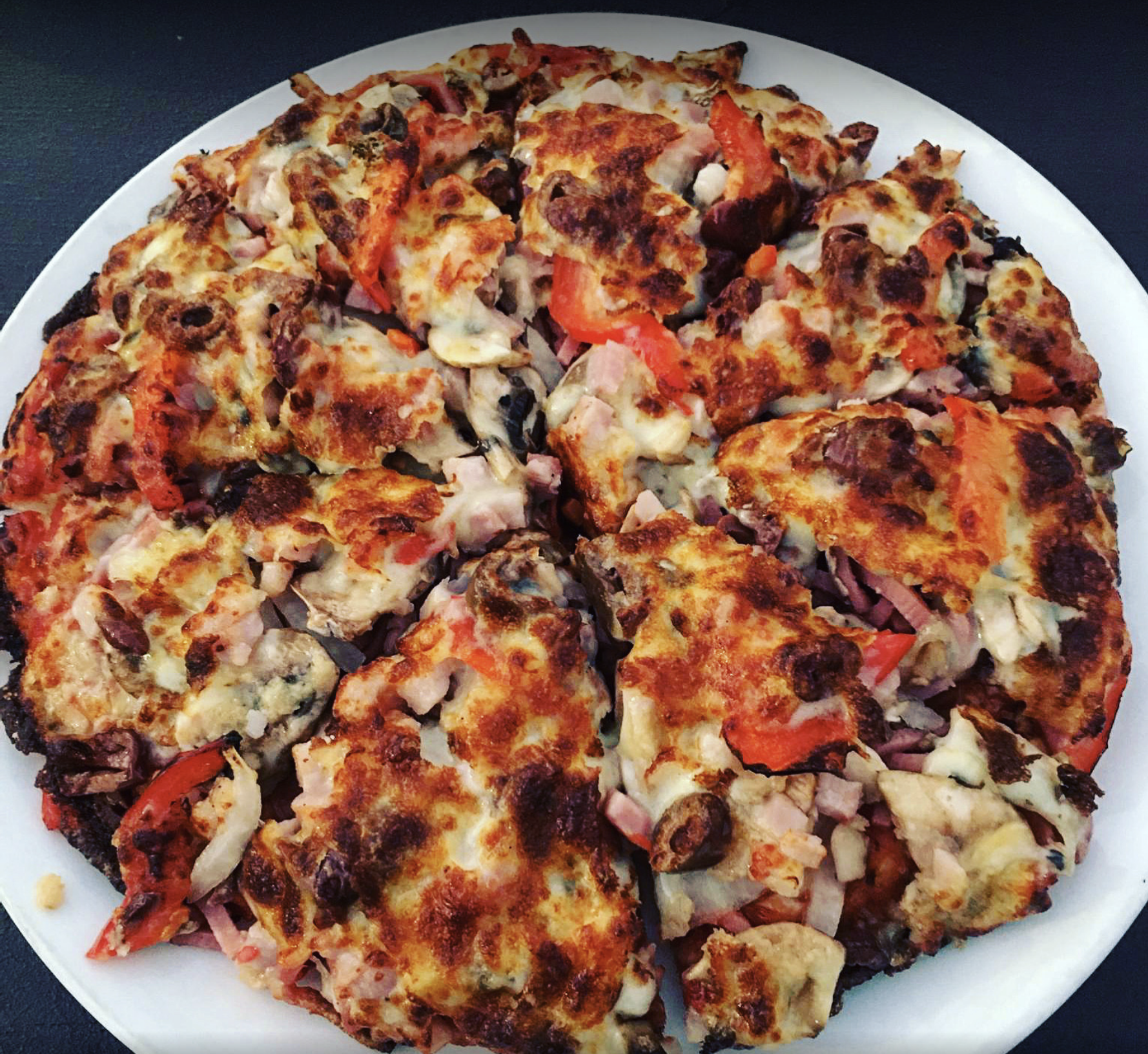 A pizza with a lot of toppings is on a white plate — Bella M Pizzas in Bundaberg North, QLD