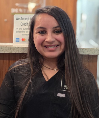 Smiling person in black scrubs standing indoors by a reception counter.