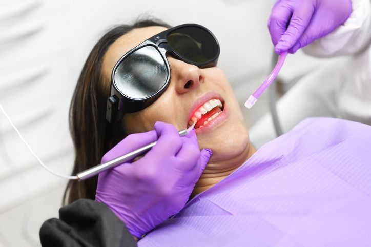 Dentist examining patient’s open mouth with mirror and tool, wearing purple gloves and mask