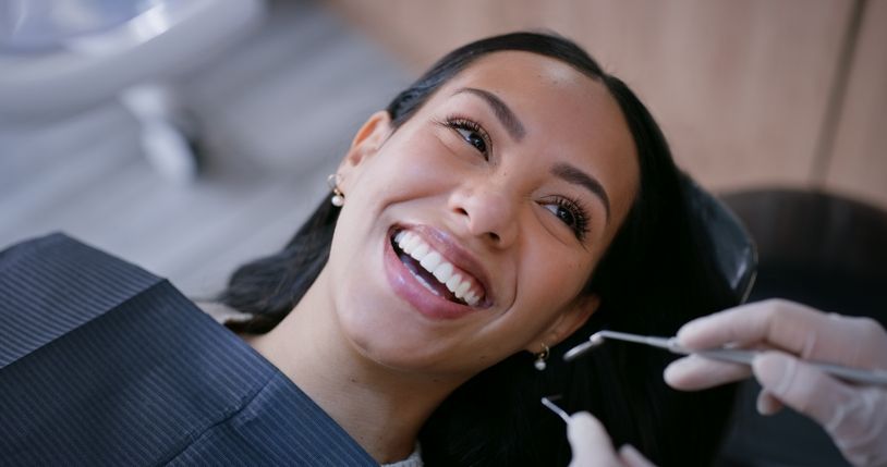 Smiling dental patient in chair while dentist uses tools during exam