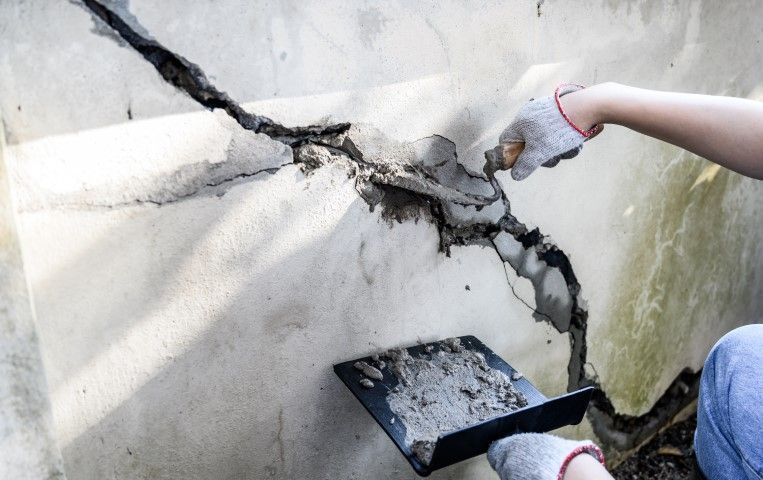 Worker repairing a large crack in a concrete wall.