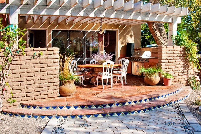 Stone outdoor pavilion with a dark wooden roof, built-in grill, and bench seating.