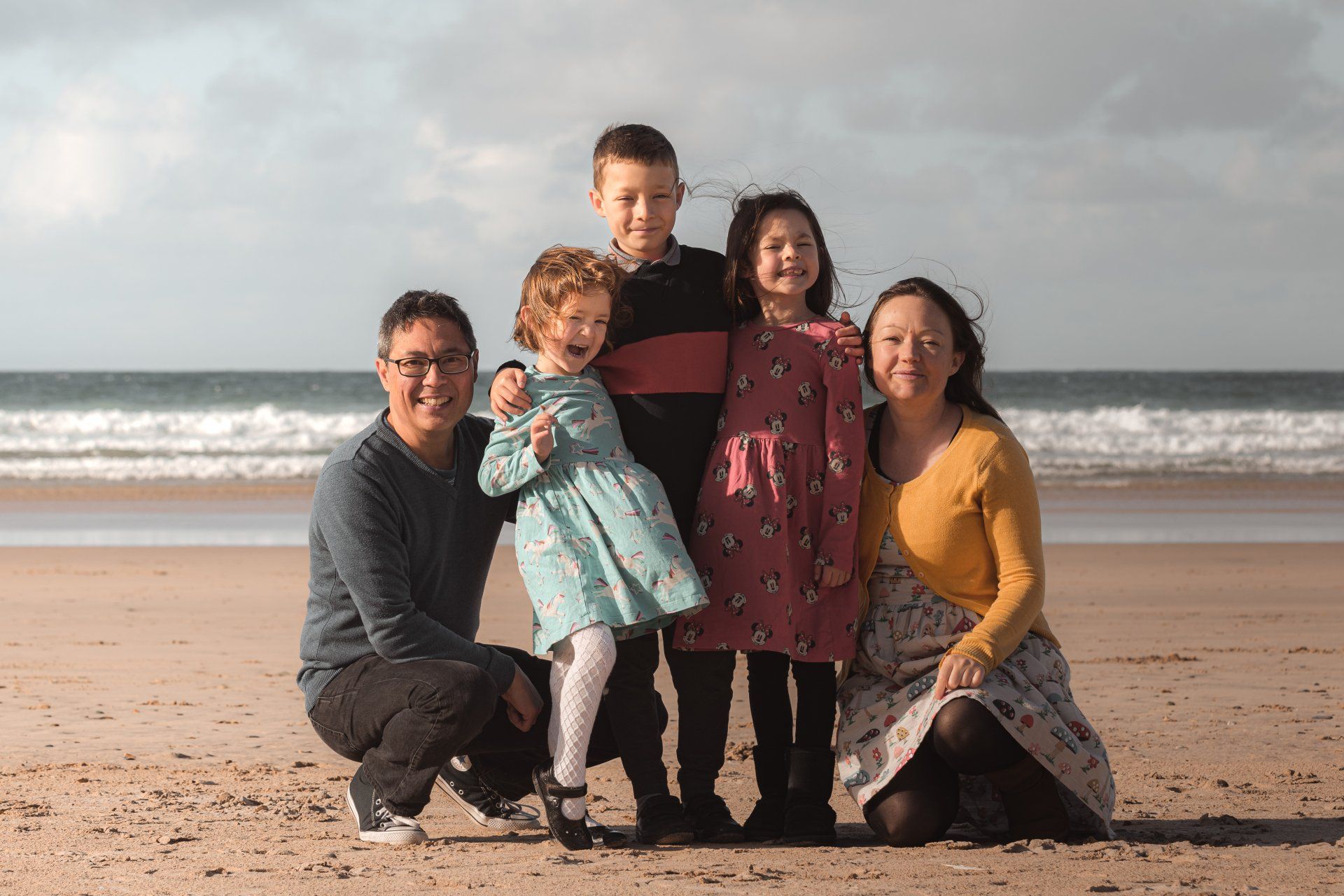 Lisa with her partner and three children smiling on a beach at sunset