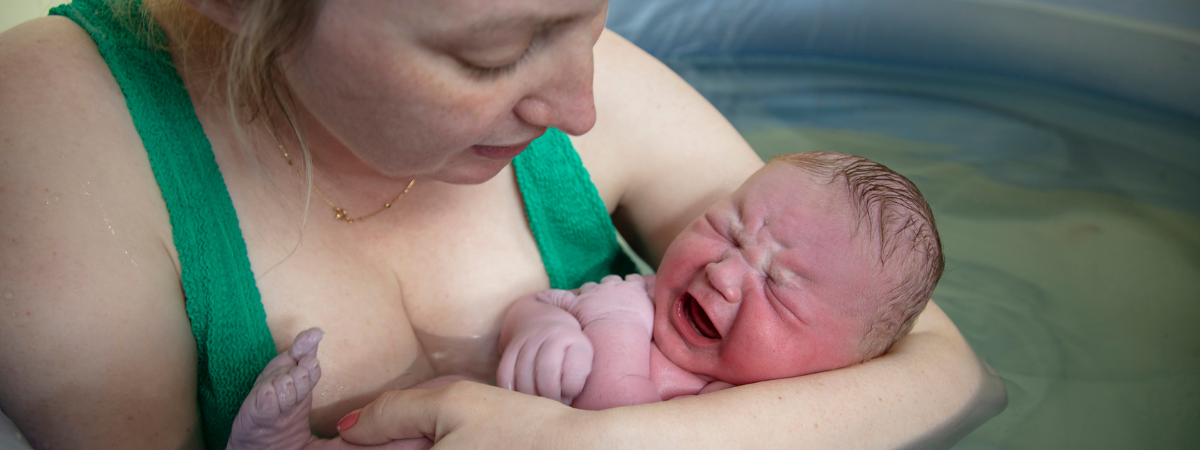 Parent holding their newborn baby in a birth pool shortly after birth