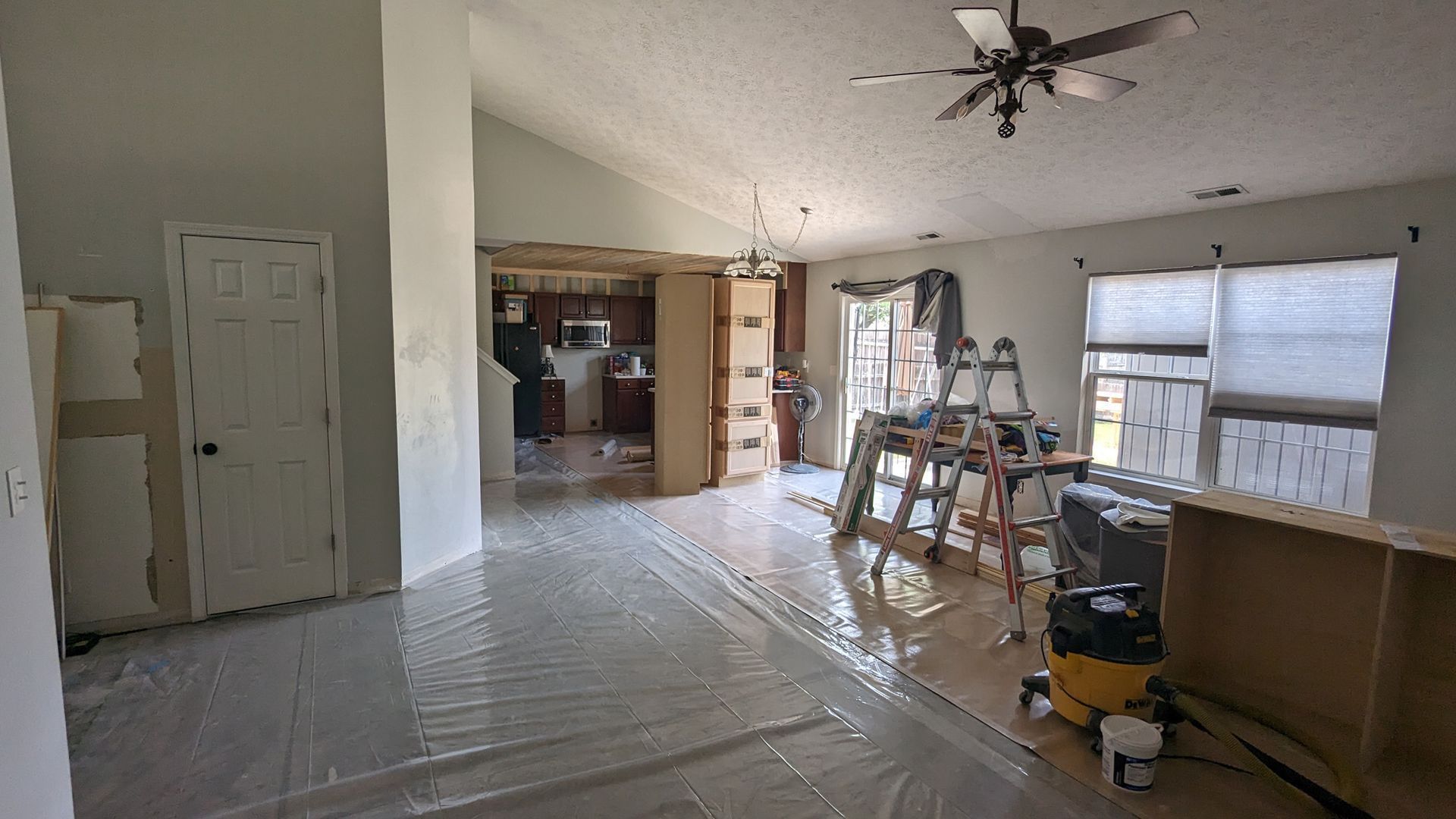 A room under renovation with drop cloths on the floor, construction ladders, a shop vacuum, and visible wall work.