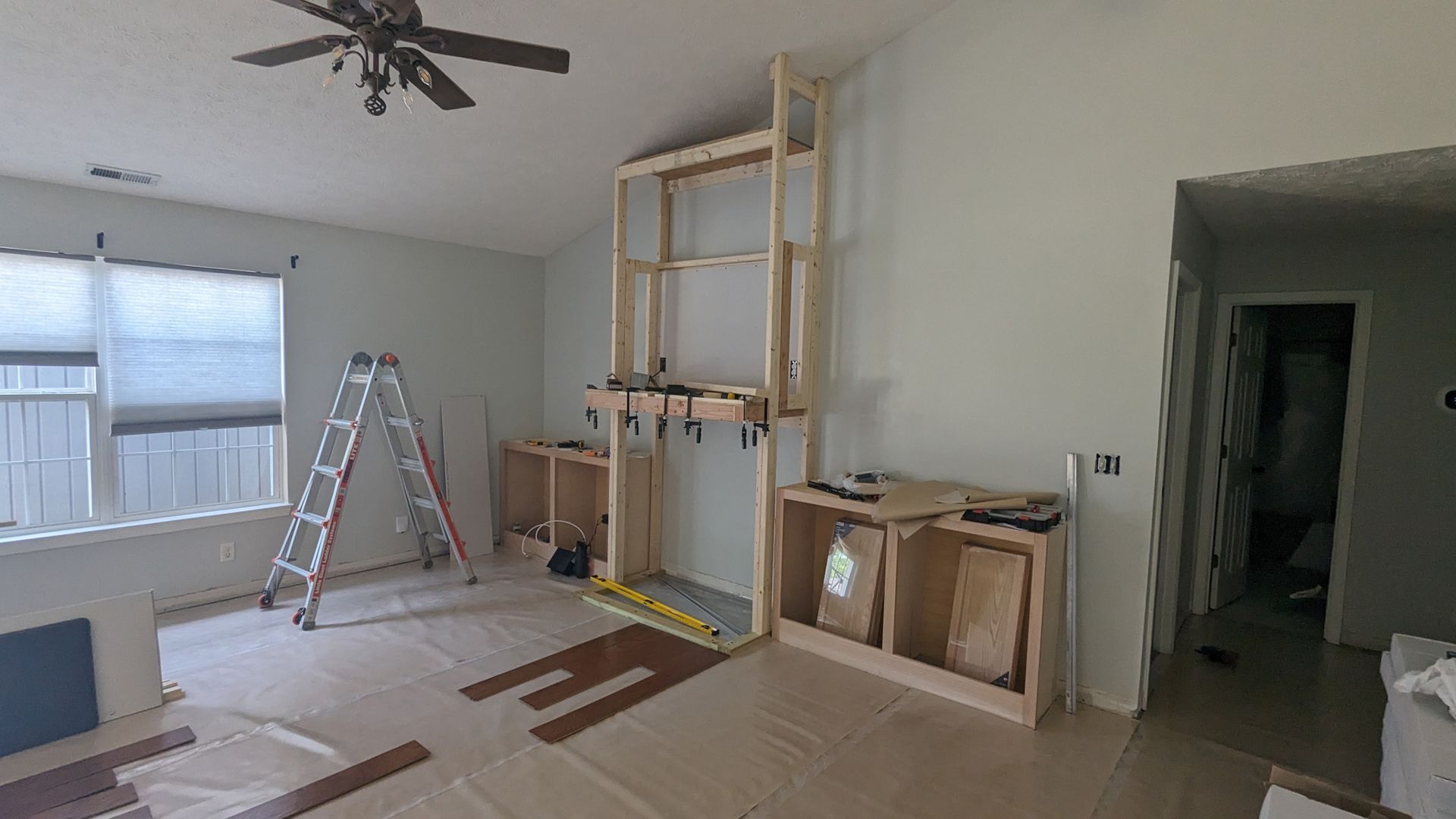 A room under construction with a wooden fireplace frame and built-in cabinets being built on a wall, with a ladder nearby.