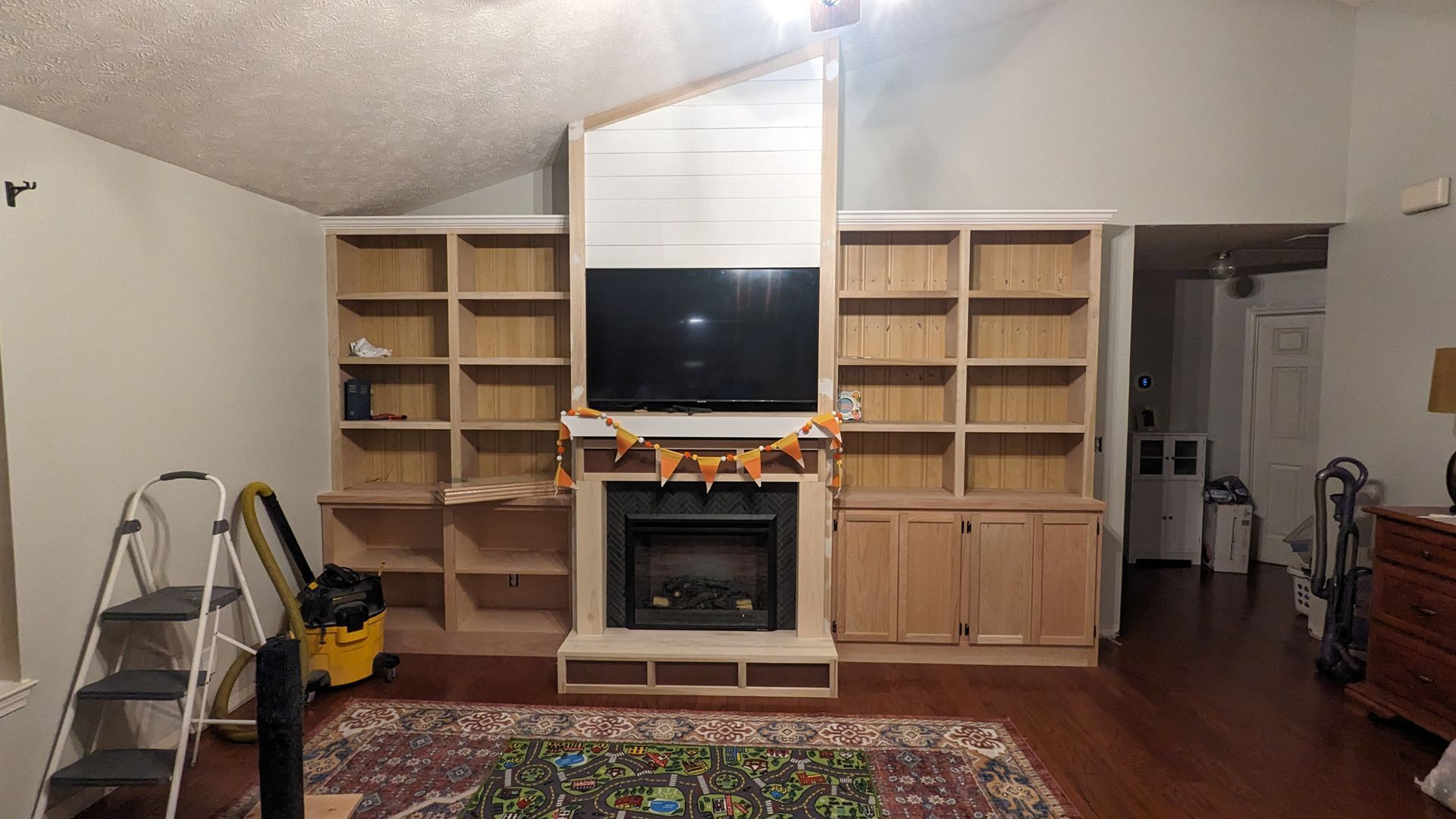Built-in light wood bookshelves surround a fireplace with a mounted television and shiplap above it in a living room.